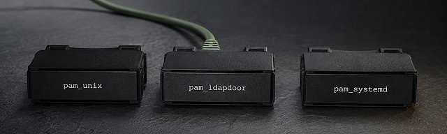 Drei mattschwarze Authentifizierungs-Modul-Cartridges in einer Reihe auf slate-grauer Oberfläche, zwei mit identischen Distribution-Labels, das mittlere subtil anders mit minimaler Label-Verschiebung und einem sage-grünen Patch-Kabel, das nach hinten links aus dem Bild läuft — Metapher für die Substitution eines PAM-Moduls durch eine schwer erkennbare Backdoor, kühles Studiolicht.