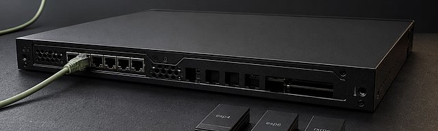 Mattschwarze Server-Edge-Box, ein sage-grünes Patch-Kabel verbindet einen aktiven Port; daneben auf der Slate-Oberfläche drei separierte Modul-Cartridges mit Mono-Labels esp4, esp6, rxrpc — Metapher für bewusst geblacklistete Kernel-Module als Mitigation, kühles Studiolicht.