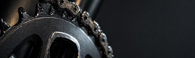 Nahaufnahme einer frisch geölten Fahrradkette und Kettenblatt mit scharfen Details im Studiolicht.