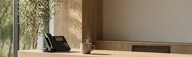 Aufgeräumter moderner Empfangstresen mit Telefon und Kaffeetasse im hellen Tageslicht.