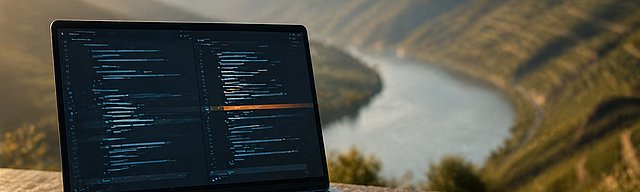Laptop auf Stein im Weinberg, Code-Diff mit warmer Markierung, Morgenlicht.