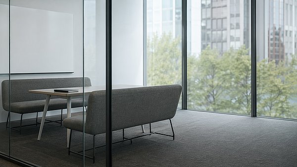 Aufgeräumter moderner Besprechungsraum hinter einer Glaswand mit leerer Whiteboard-Wand und zwei gegenüberstehenden Sitzbänken.