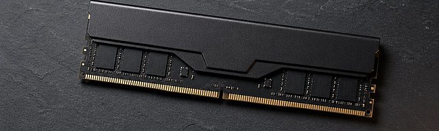 Mattschwarzer DDR5-RAM-Riegel liegt diagonal auf dunkler Schieferoberfläche, von links kühl beleuchtet, mit sichtbaren goldenen Kontakten und kurzem Schatten nach rechts.