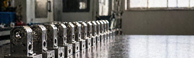 Reihe identisch gefertigter Metallbauteile exakt ausgerichtet auf einer Werkbank im Seitenlicht.