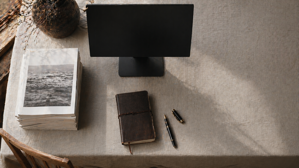 Aufgeräumter Redaktions-Arbeitsplatz von oben mit gestapelten gedruckten Magazinen neben einem ausgeschalteten Monitor.