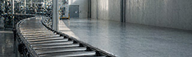 Industrielles Förderband mit Rollen in leichter Bewegungsunschärfe in einer hellen Fabrikhalle.